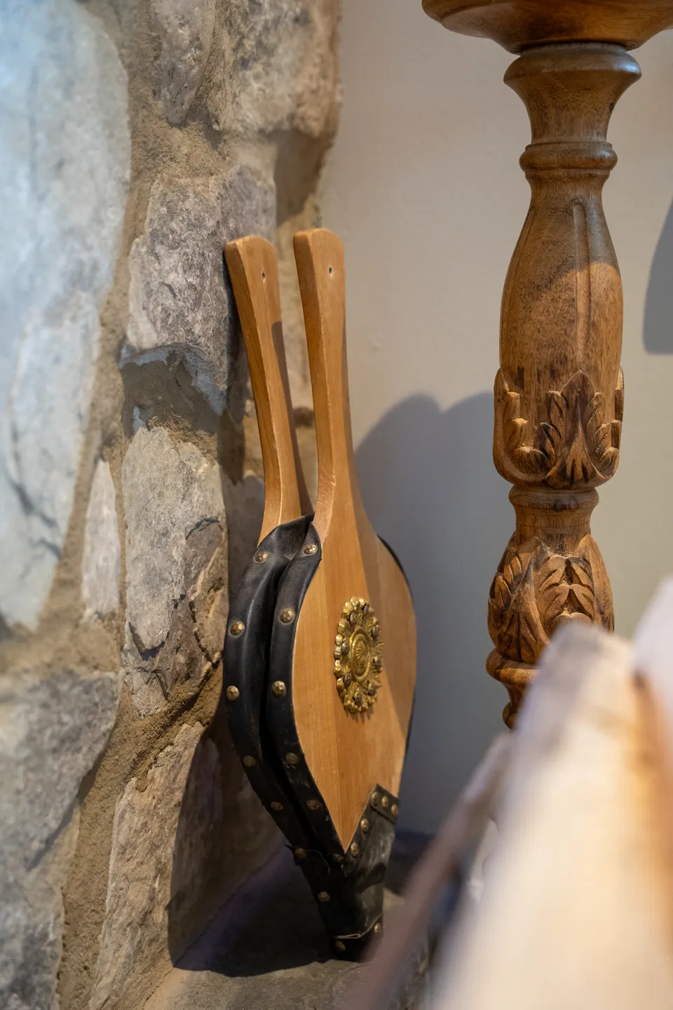 Riveted leather-and-brass bellows against the fieldstone hearth, beside a hand-carved candlestick.