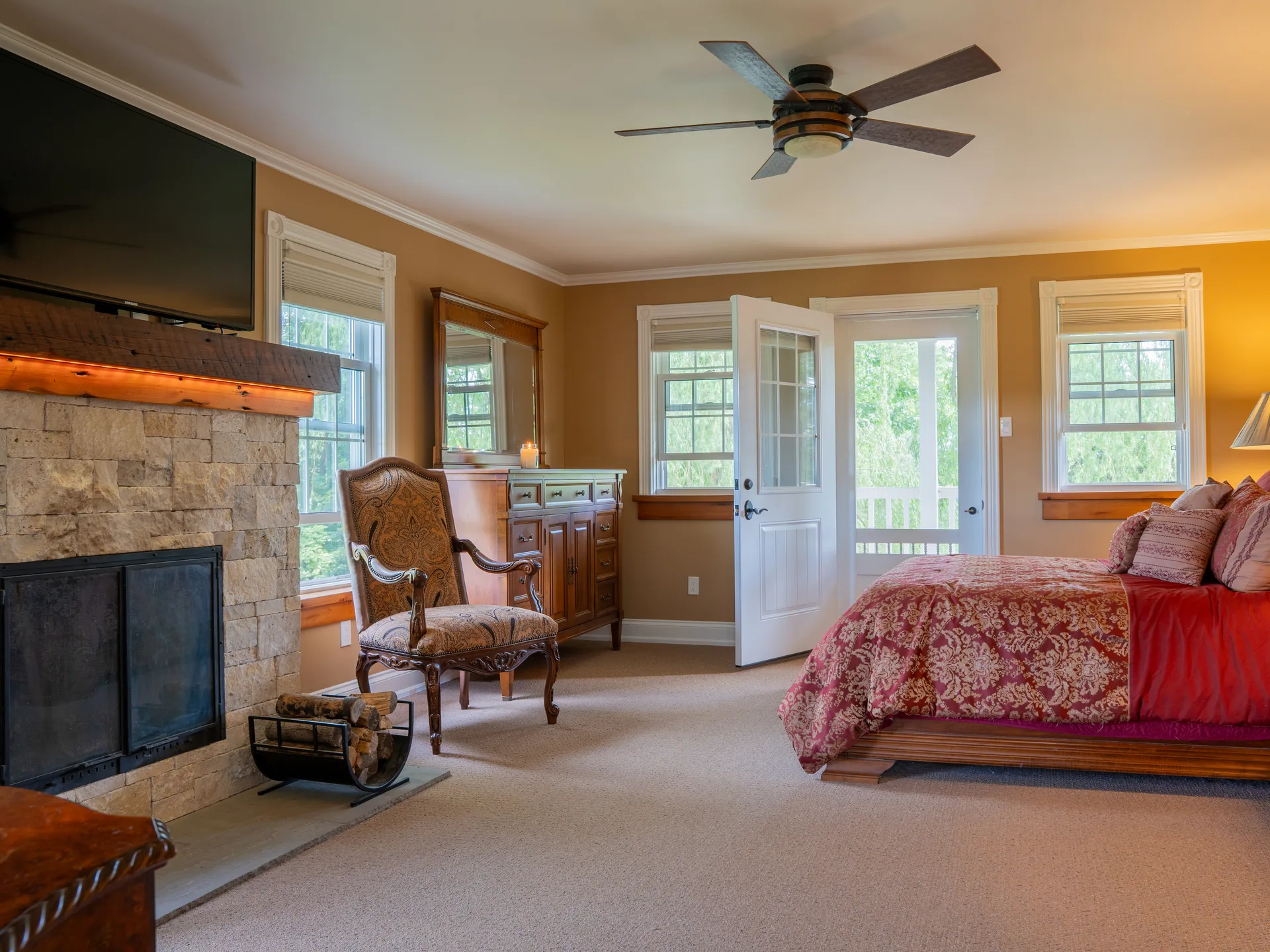 Primary bedroom viewed from the fireplace across to the bed and the open French door to the porch.